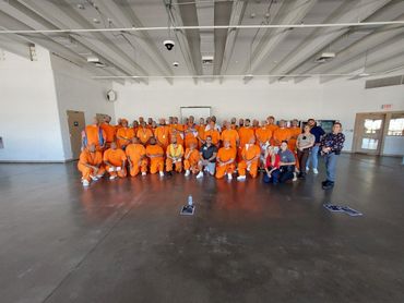 Group photo of inmates and staff in a large room, inmates wearing orange uniforms.