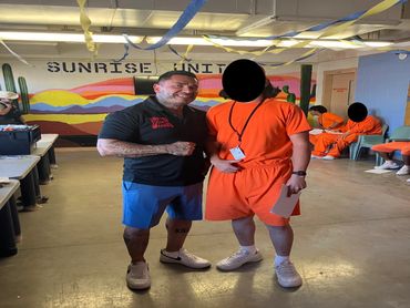 Two men posing in a decorated room with a "SUNRISE UNIT" mural behind them.