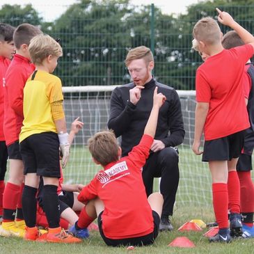 Youth soccer coach instructs attentive kids during training session on the field.