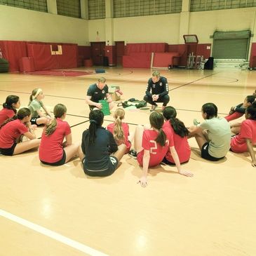 Girls' basketball team receiving coaching in a gymnasium.