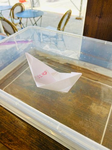 A paper boat labeled S.S. MCP floating in a clear water container.