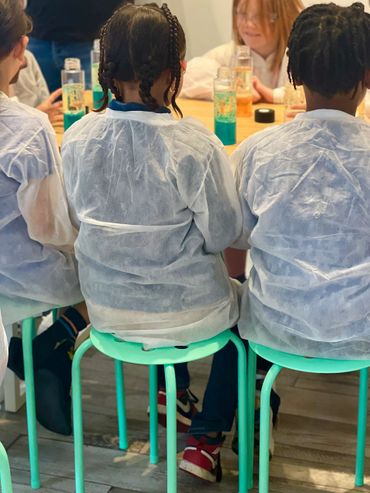 Children in lab coats sitting on stools at a science table.