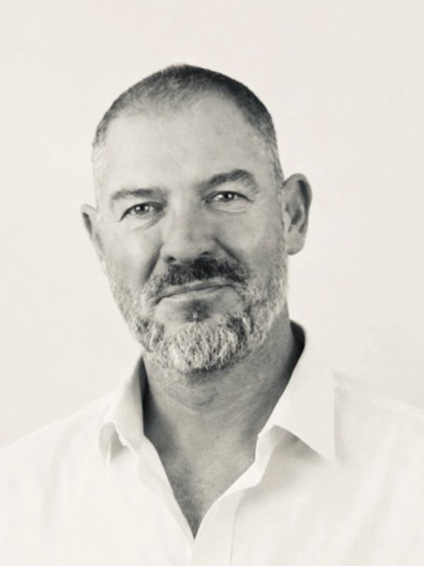 Portrait of a mature man with a beard and white shirt, smiling gently.