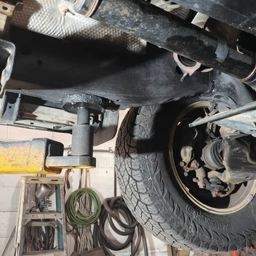 Underside of a vehicle lifted in a garage with visible tire, exhaust pipe, and tools.