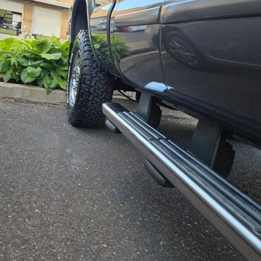 Close-up of a black truck's side and rugged tire on pavement.