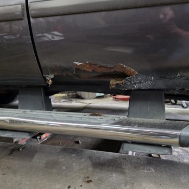 Rust and damage on the lower side of a car door next to a chrome side step.