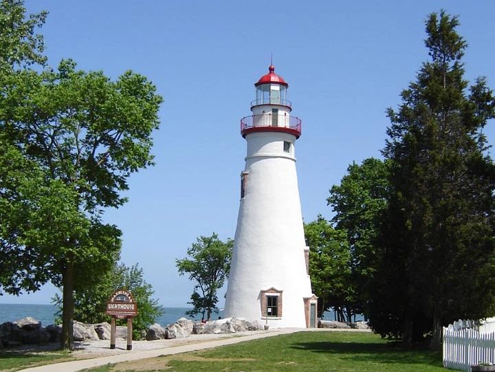 A white and red lighthouse surrounded by trees and a clear blue sky.