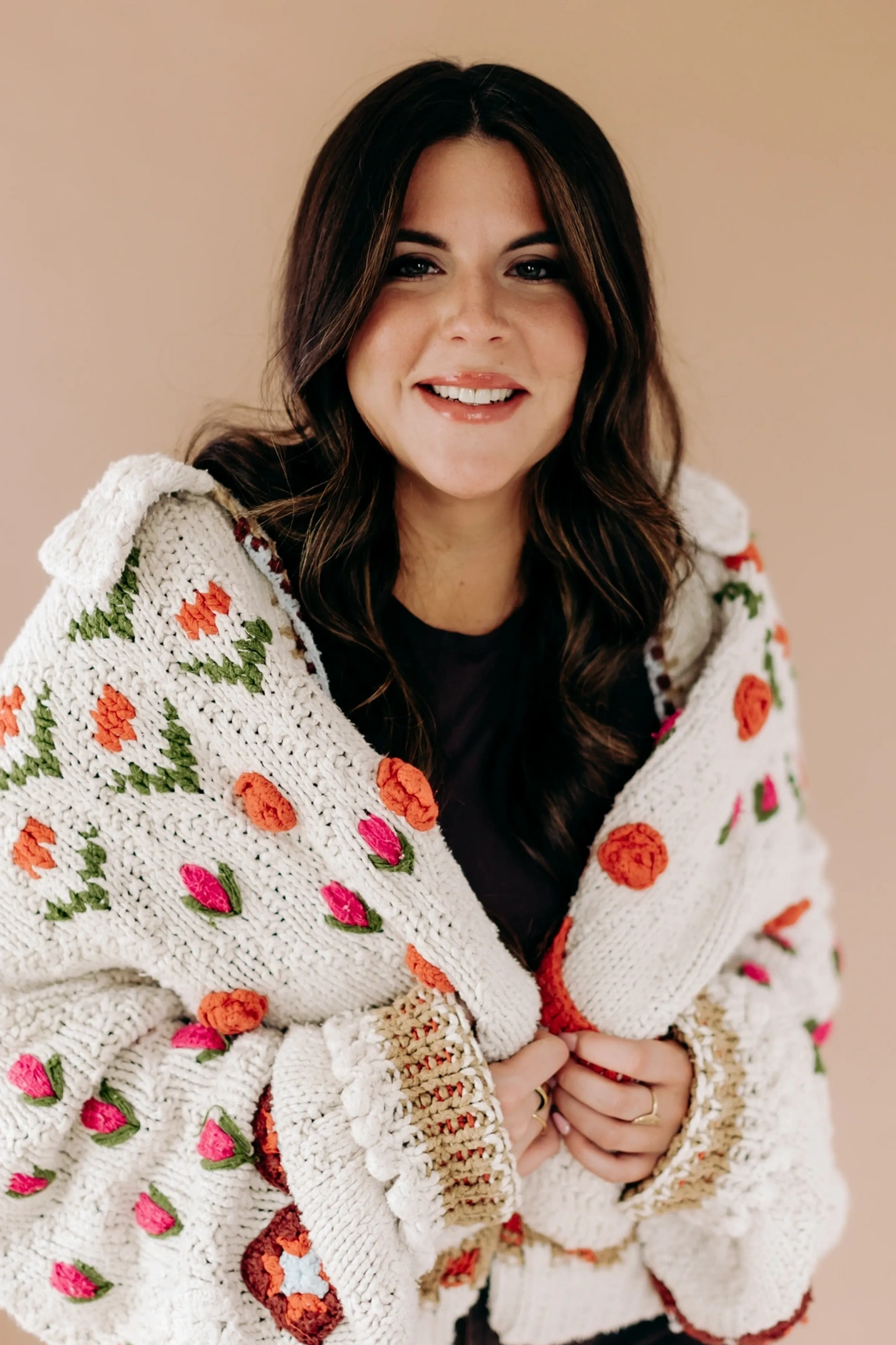 Smiling woman wrapped in a colorful knitted sweater with floral patterns.
