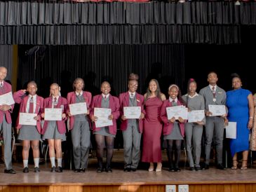 Group of students and adults holding certificates on stage.