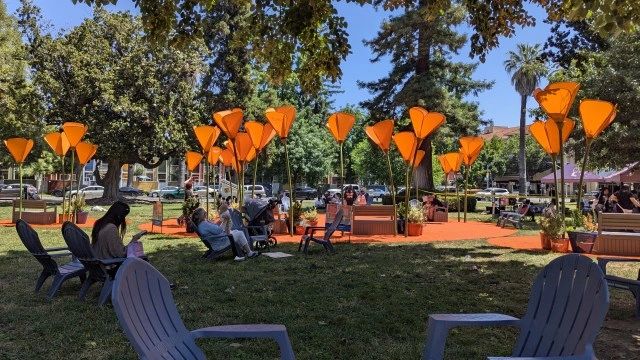 People sitting in a park with orange lanterns and chairs under trees.