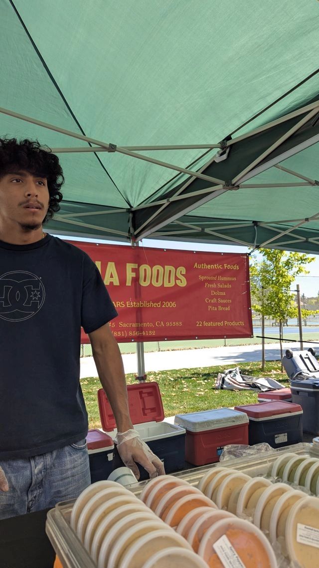 A vendor at a food stall with containers of food under a canopy.