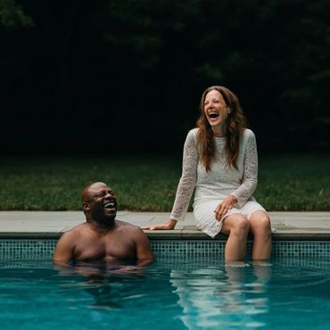 A joyful couple laughing together by the poolside, sharing a happy moment.