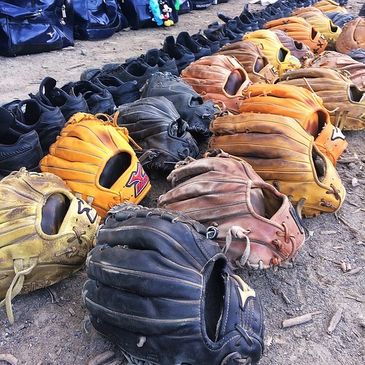 Base ball gloves, cleats and bags lined up on the ground.