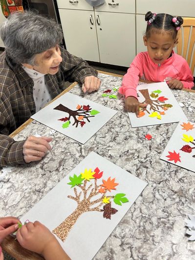 Elder and child create paper leaf trees together.