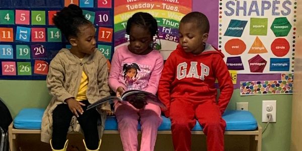 Three kids sitting on a bench in a colorful classroom setting.