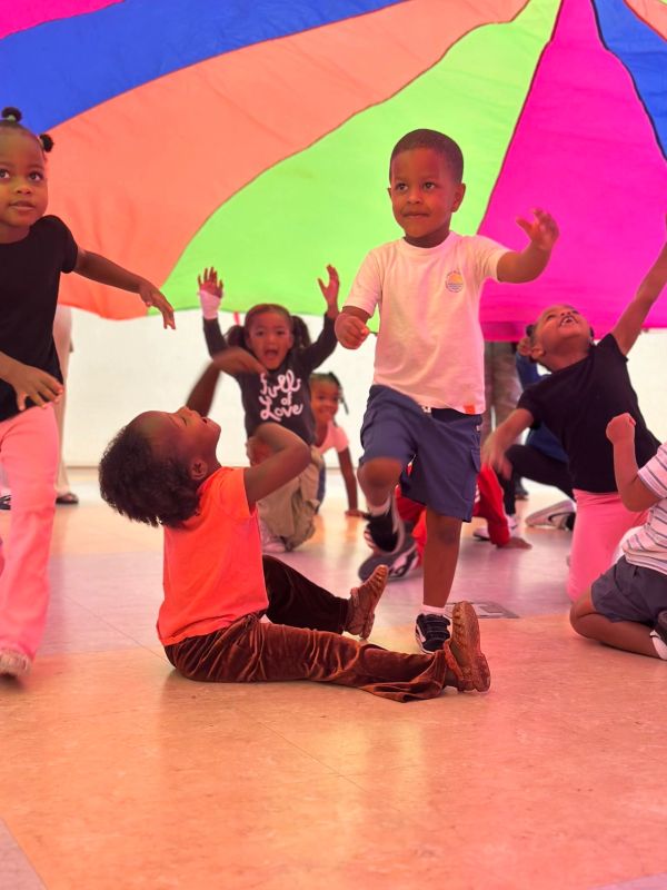 Children playing with a colorful parachute indoors.