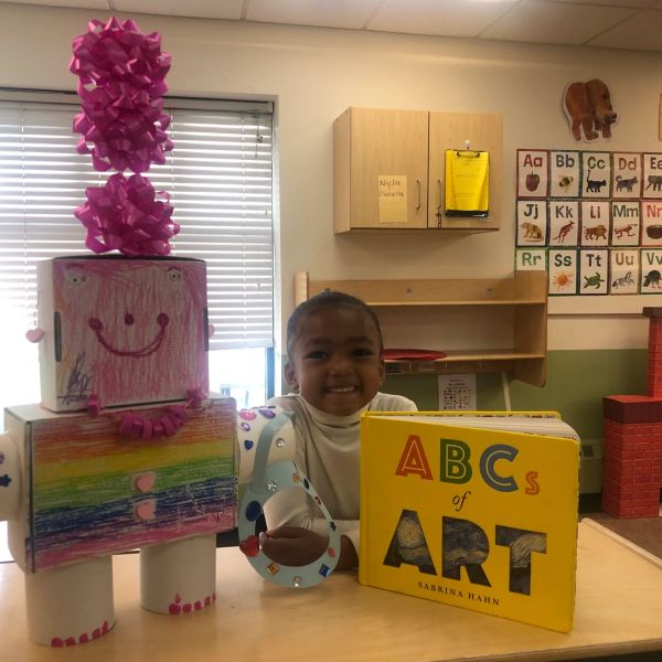 Happy child with colorful robot and ABC book in classroom.