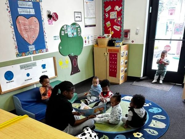 Teacher reading to a group of toddlers in a colorful classroom.