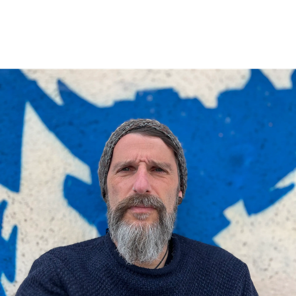 Man with a gray beard and knit hat against a blue and white graffiti wall.