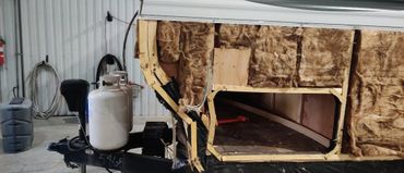 Partially stripped trailer wall reveals insulation and wooden frame inside.