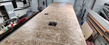 A large wooden surface with cutouts in a workshop surrounded by RVs.