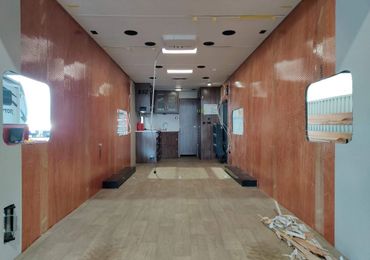 Interior of an unfinished RV with exposed walls and basic kitchen setup.