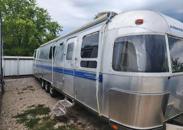 A silver Airstream Classic trailer parked on gravel near a fence.