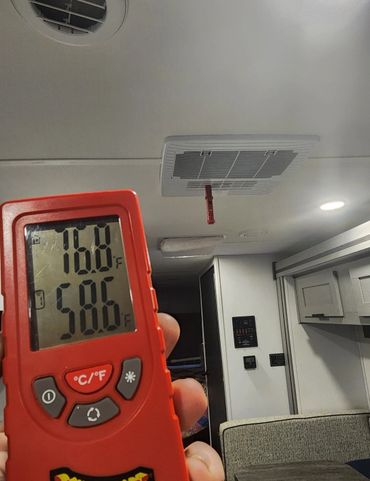 A digital thermometer showing temperatures inside a room with ceiling vents.