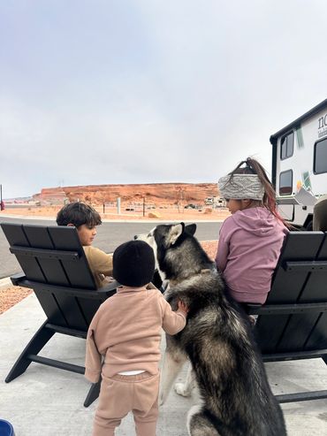Three children and a husky dog enjoying outdoor seating near desert landscape.