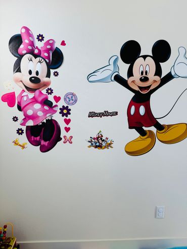 Wall decals of Minnie Mouse and Mickey Mouse with colorful hearts and flowers.