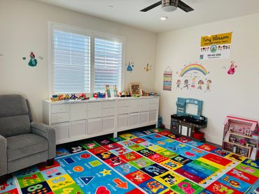 Colorful and organized child care room with toys, educational carpet, and comfy chair.