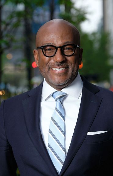 Blackman wearing glasses smile navy-blue suite outside