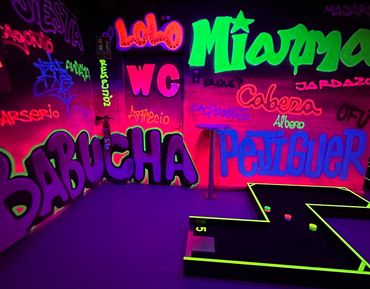 Vibrant neon graffiti walls illuminate an indoor mini-golf course with colorful pucks and a fire extinguisher.