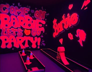 A neon-lit Barbie-themed mini golf course with vibrant pink graffiti and obstacles.
