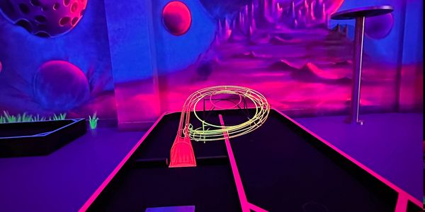Neon-lit mini golf hole with space-themed mural in the background.