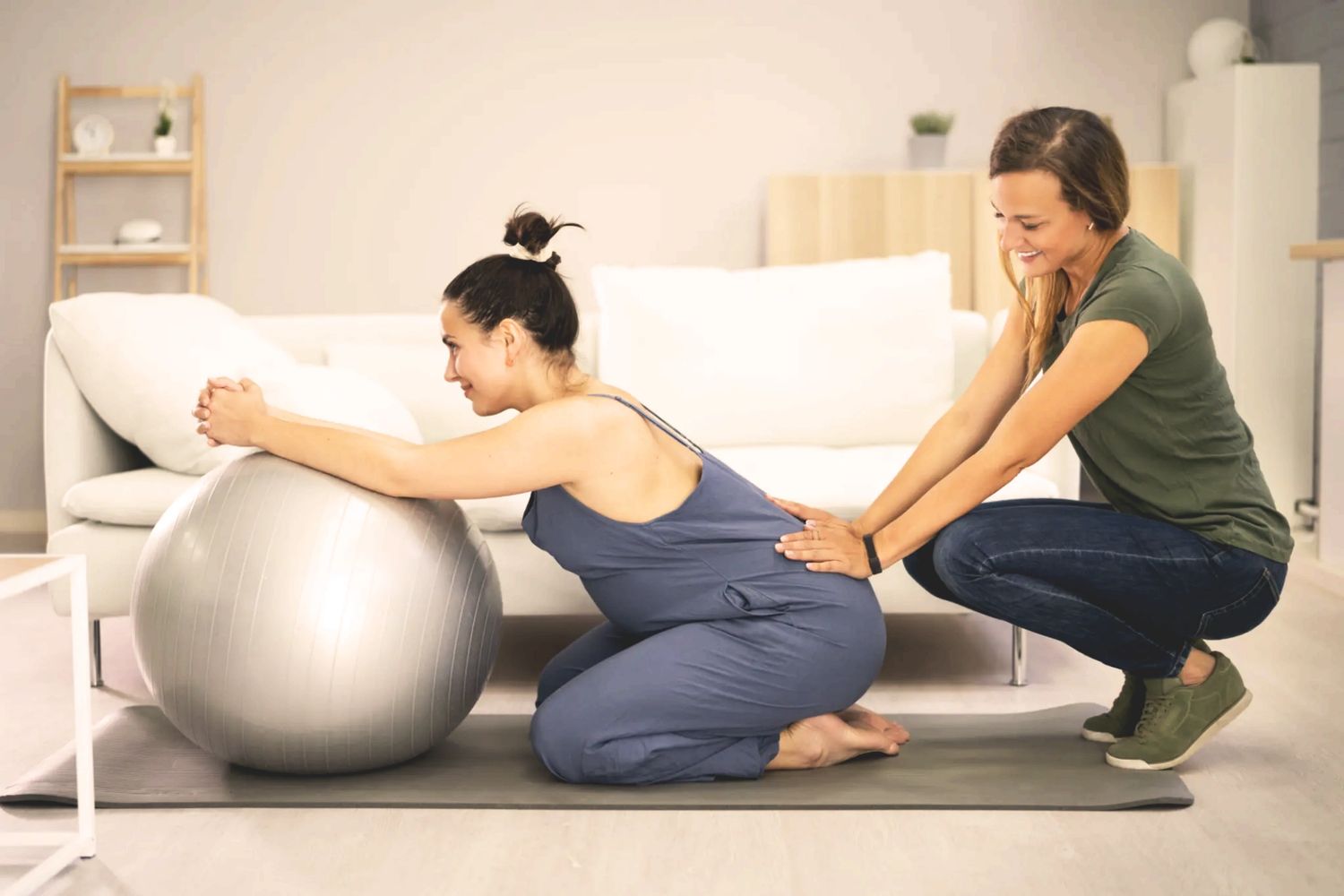Doula assisting pregnant client with a birthing ball