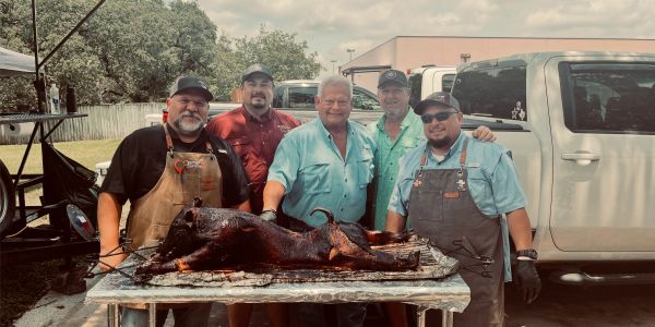 Five men posing with a roasted pig outdoors.