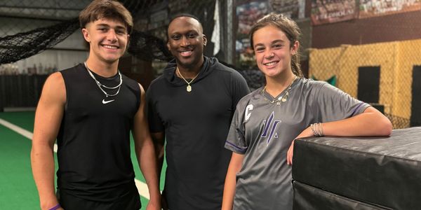 Three smiling young athletes posing indoors on a sports field.