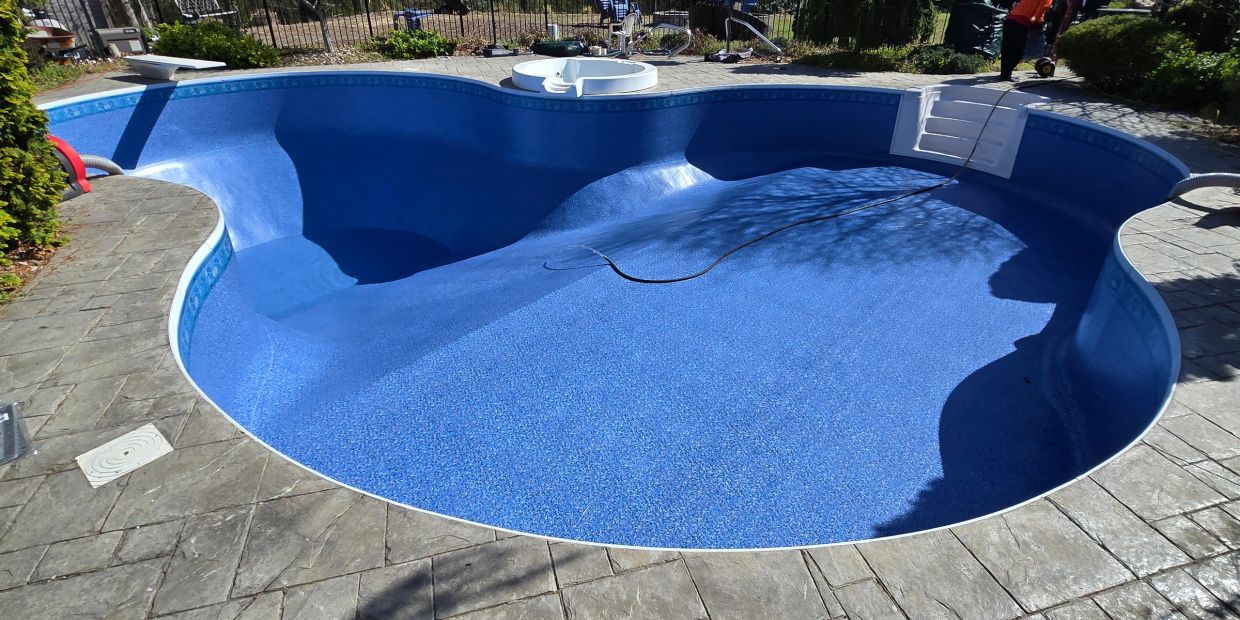 Empty blue swimming pool with a small attached hot tub and surrounding stone pavement.