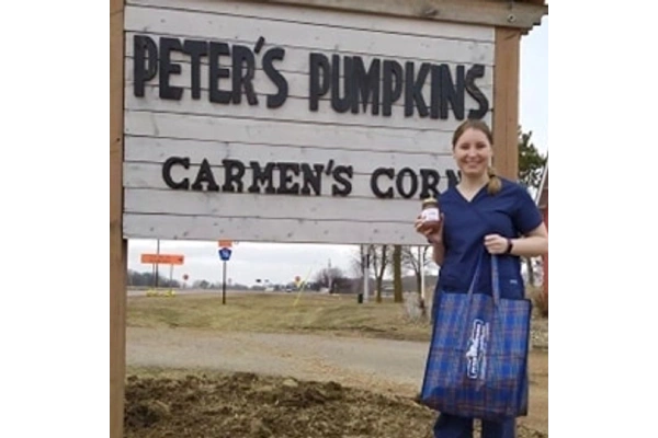 A woman posing with a jar full of a salsa near a shop