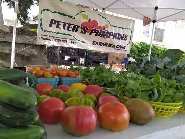 A farmers market stall with a banner for Peter's Pumpkins Carmen's Corn, featuring fresh produce.