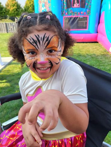 Smiling child with tiger face paint and colorful outfit at a fun outdoor event.