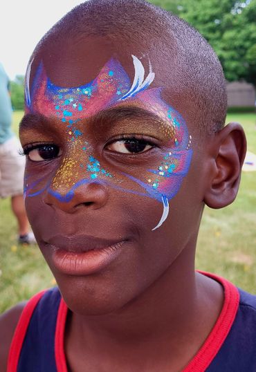Boy with colorful face paint in a park setting.
