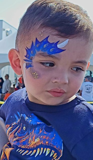 Young boy with blue dinosaur face paint and matching dinosaur shirt.