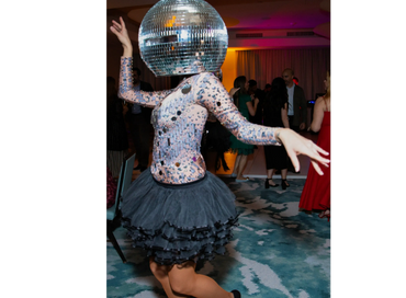 Person dancing with a disco ball helmet and a frilly black skirt at a party.