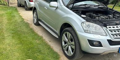 Silver SUV with its hood open parked on a driveway near grass.