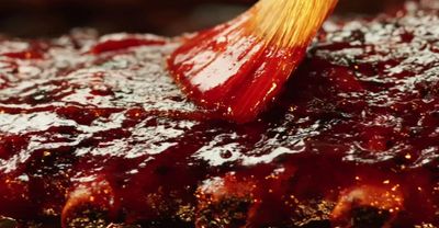 A brush spreading barbecue sauce over grilled meat.