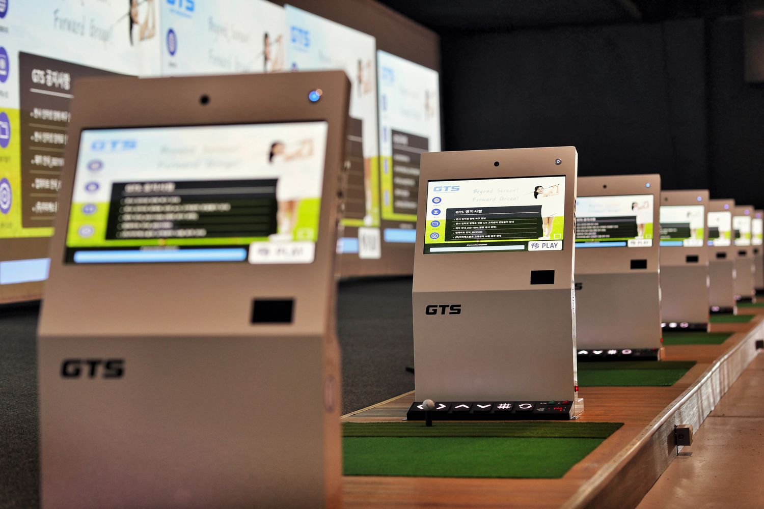 A row of high-tech golf simulators with digital screens and golf balls ready for play.