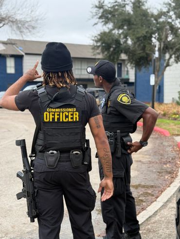Two commissioned officers in tactical gear stand on a street.
