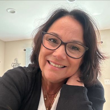 A smiling woman wearing glasses and a black sweater, posing indoors.